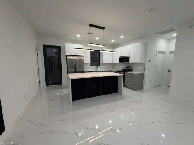 Kitchen with white cabinets, a center island, appliances with stainless steel finishes, hanging light fixtures, and modern cabinets
