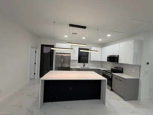 Kitchen with modern cabinets, stainless steel appliances, pendant lighting, white cabinets, and a center island