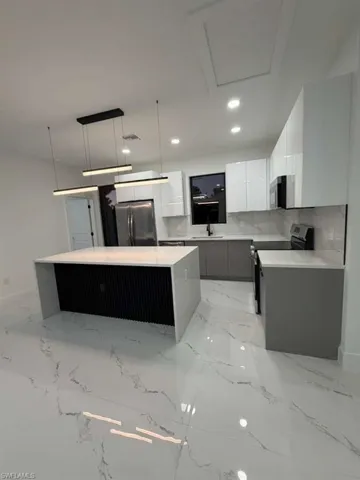 Kitchen featuring a kitchen island, white cabinetry, modern cabinets, decorative light fixtures, and appliances with stainless steel finishes