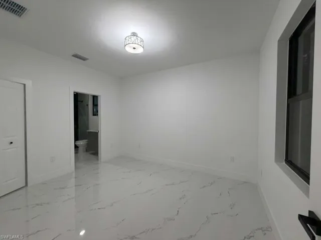 Unfurnished bedroom with light marble finish floors and connected bathroom