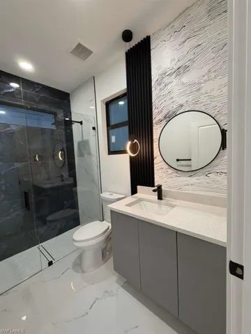 Bathroom featuring light marble finish floors, a marble finish shower, vanity, and recessed lighting