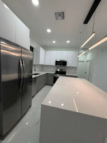 Kitchen featuring stainless steel appliances, light stone counters, modern cabinets, white cabinetry, and gray cabinets