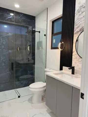 Bathroom featuring vanity, light marble finish floors, and a marble finish shower
