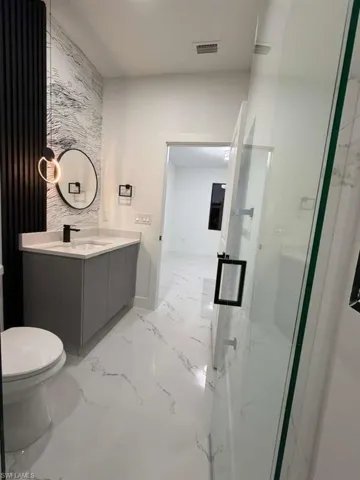 Full bath featuring vanity, a marble finish shower, and light marble finish floors