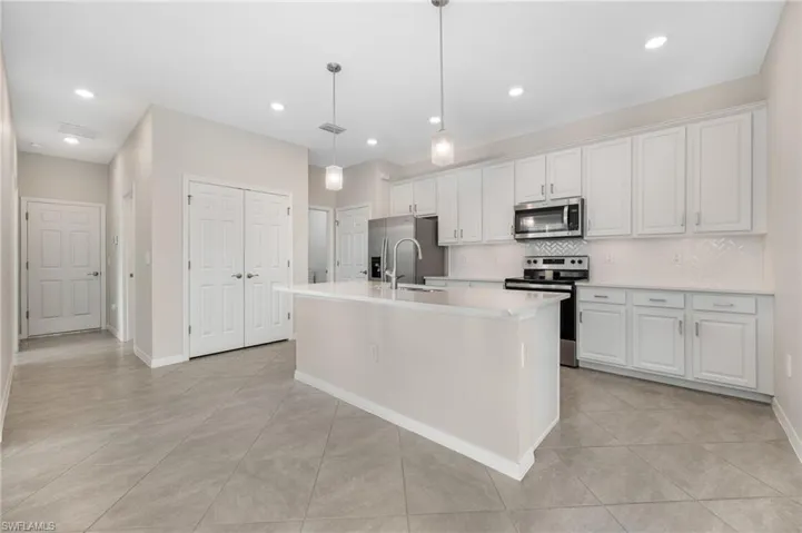 Kitchen featuring appliances with stainless steel finishes, a kitchen island with sink, light countertops, and white cabinetry