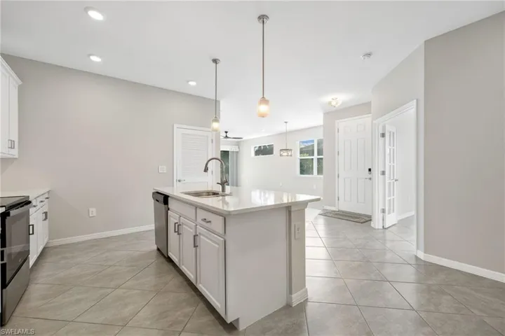 Kitchen featuring an island with sink, light countertops, white cabinetry, pendant lighting, and a sink