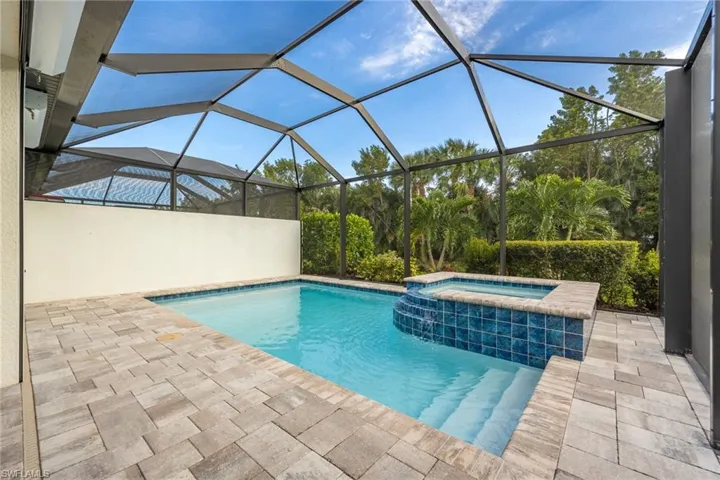 View of swimming pool featuring a pool with connected hot tub, glass enclosure, and a patio