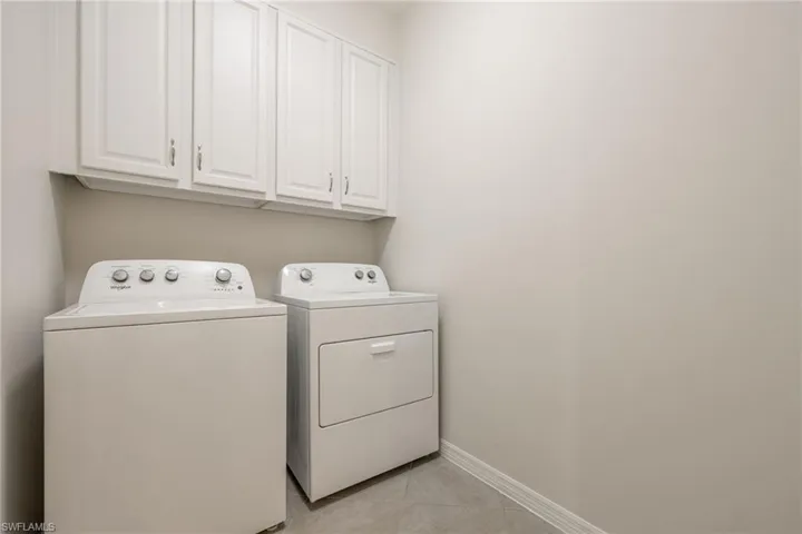 Clothes washing area with light tile patterned floors, washing machine and clothes dryer, cabinet space, and baseboards