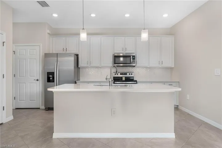 Kitchen featuring visible vents, light countertops, appliances with stainless steel finishes, a center island with sink, and pendant lighting
