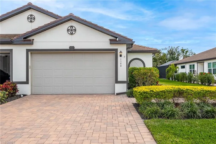 View of front facade with decorative driveway, a tiled roof, an attached garage, and stucco siding