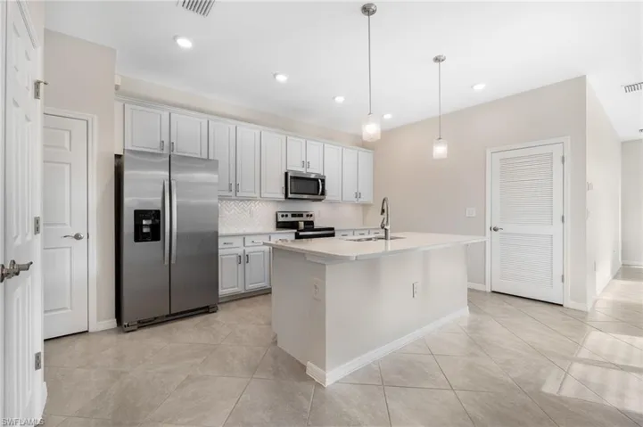 Kitchen featuring stainless steel appliances, a sink, light countertops, a center island with sink, and pendant lighting