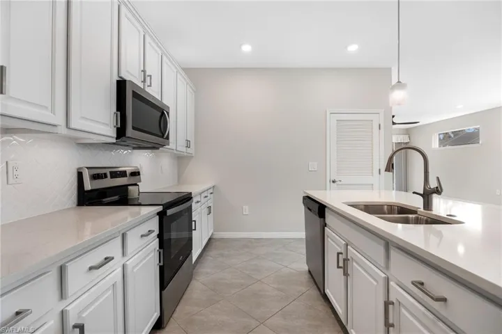 Kitchen with decorative light fixtures, appliances with stainless steel finishes, white cabinets, a sink, and light stone countertops