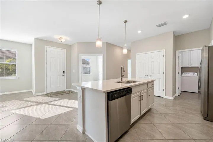 Kitchen featuring a center island with sink, stainless steel appliances, light countertops, a sink, and washer / dryer