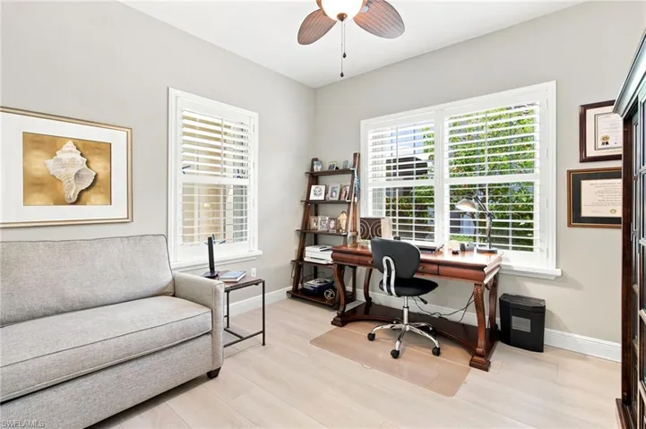 Bright room featuring light-toned wood-finish flooring, white plantation shutters, a ceiling fan with integrated lighting, and crown molding