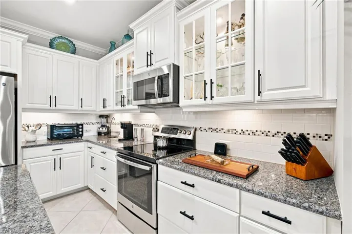 Modern kitchen featuring white cabinetry with black hardware, stainless steel appliances, and granite countertops