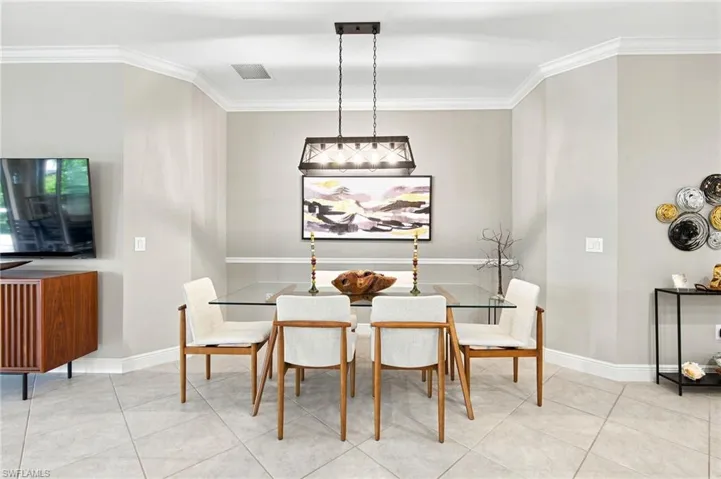 Dining area featuring crown molding, neutral wall tones, a contemporary chandelier, a glass-top dining table, and tile flooring