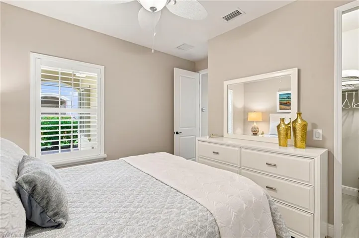 Bedroom featuring a window with white louvered shutters, a ceiling fan with light fixture, light neutral wall paint, and a built-in closet with shelving