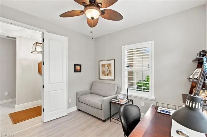 Neutral-toned room featuring light wood-finish flooring, a ceiling fan with light fixture, and a window with plantation shutters