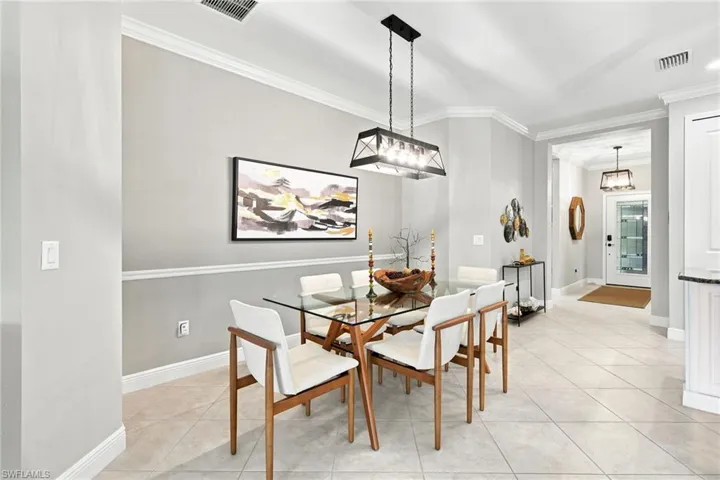 Dining area featuring a contemporary linear chandelier, crown molding, chair rail detailing, light-toned tile flooring, and a recessed entryway