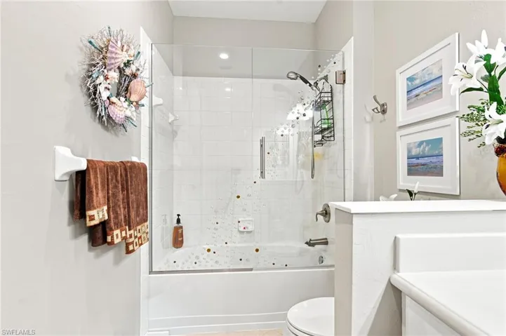 Bathroom with a combination bathtub and shower featuring a clear glass enclosure and white subway tile surround