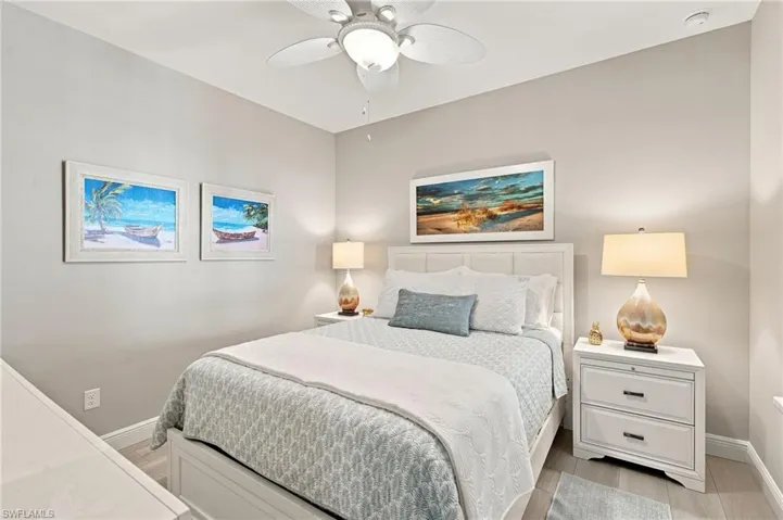 Bedroom featuring light gray walls, a white ceiling fan with integrated lighting, wood-finish flooring, and white baseboards