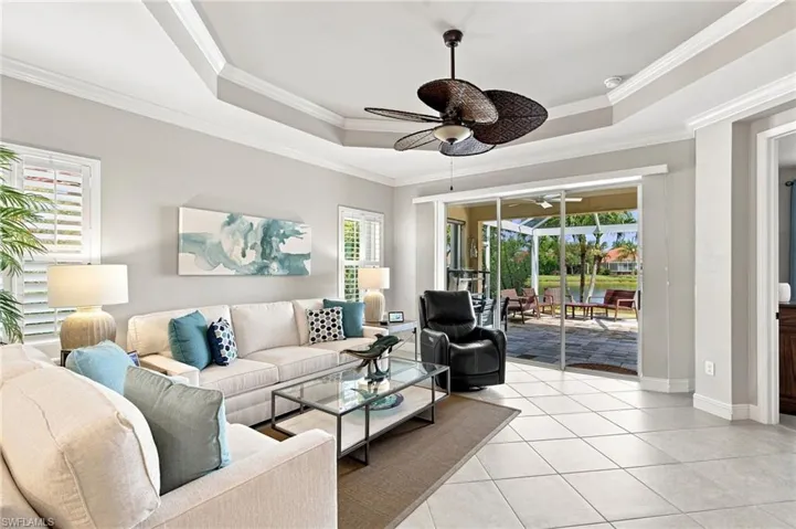 Spacious living area featuring coffered ceilings, tile flooring, plantation shutters, and sliding glass doors leading to a screened lanai with water frontage