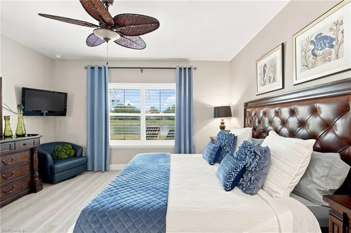 Bedroom featuring light-tone wood-finish flooring, a window with horizontal blinds, a ceiling fan with light fixture, and neutral-tone walls