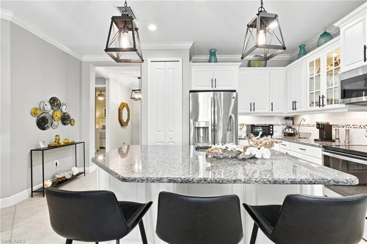Kitchen featuring a granite-topped island with seating, white cabinetry, stainless steel appliances, and pendant lighting