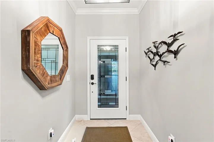 Entryway with a decorative leaded glass door, crown molding, and light-toned tile flooring