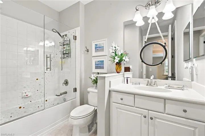 Bathroom featuring a built-in tub with a glass shower enclosure, white tile surround, white vanity cabinetry with a single sink, light-toned countertop, and a large wall-mounted mirror