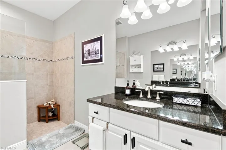 Double vanity featuring white cabinetry with black hardware, dark granite countertops, and dual undermount sinks