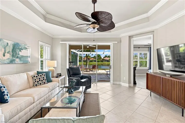 Spacious living area featuring tile flooring, a tray ceiling with a ceiling fan, and plantation shutters