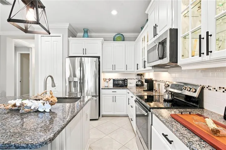 Kitchen featuring white shaker cabinetry, stainless steel appliances, granite countertops, a subway tile backsplash with decorative accents, and tiled flooring