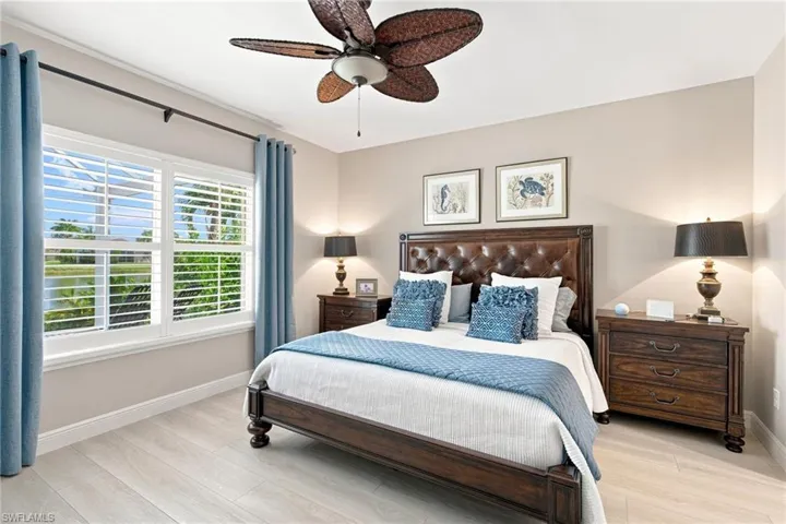 Bedroom featuring light wood-finish flooring, a ceiling fan, and window with plantation shutters