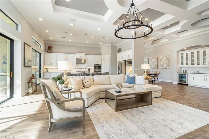 Living room featuring beverage cooler, coffered ceiling, an inviting chandelier, ornamental molding, and light wood-type flooring