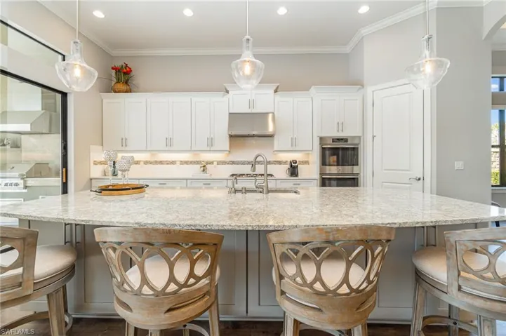 Kitchen featuring white cabinets, pendant lighting, light stone countertops, and a large island