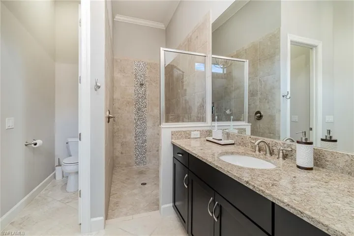 Bathroom with walk in shower, tile patterned flooring, toilet, vanity, and ornamental molding