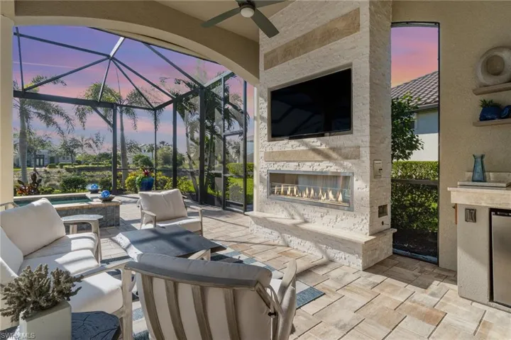 View of patio with an outdoor stone fireplace, ceiling fan, a lanai, and a jacuzzi