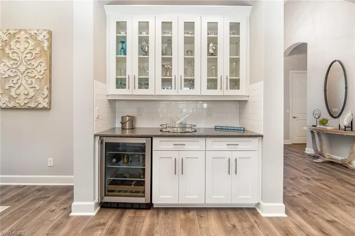 Bar with stone countertops, white cabinetry, wine cooler, and light hardwood / wood-style flooring