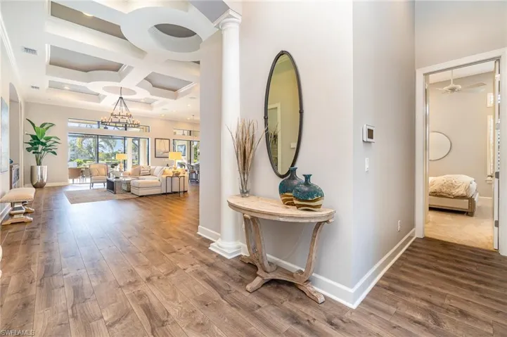 Corridor featuring ornate columns, wood-type flooring, coffered ceiling, and a notable chandelier
