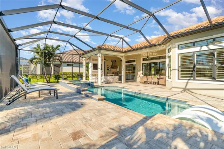 View of swimming pool featuring glass enclosure, ceiling fan, a patio, and an in ground hot tub
