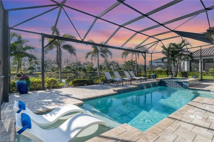 Pool at dusk featuring a lanai, a patio area, and an in ground hot tub