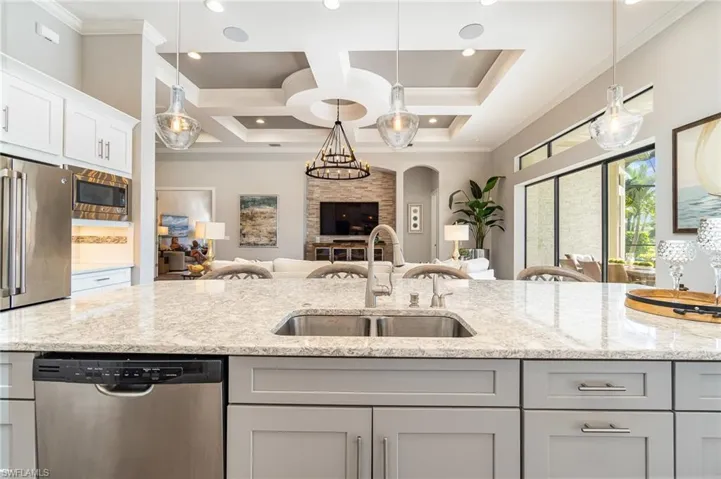 Kitchen with light stone counters, coffered ceiling, stainless steel appliances, sink, and gray cabinets
