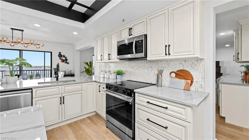 Kitchen featuring light stone countertops, stainless steel appliances, white cabinets, light wood finished floors, and hanging light fixtures