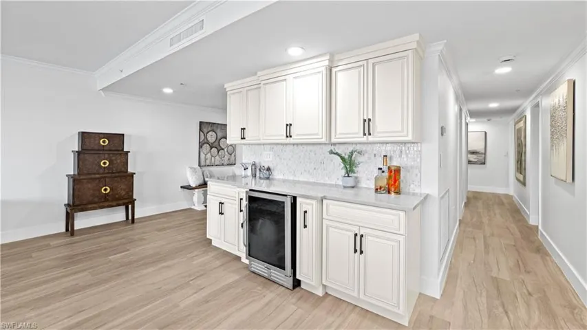 Bar featuring crown molding, light stone countertops, beverage cooler, backsplash, and white cabinetry