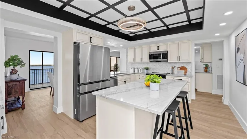 Kitchen with stainless steel appliances, light stone counters, a breakfast bar area, a kitchen island, and light wood-style floors