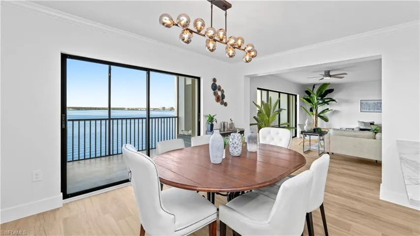 Dining room with a chandelier, a water view, light wood-style flooring, ceiling fan, and ornamental molding
