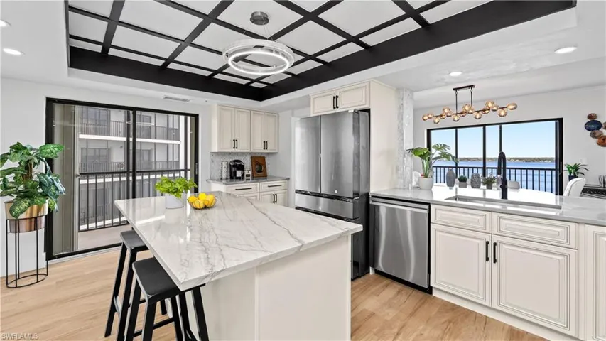 Kitchen with stainless steel appliances, a raised ceiling, a kitchen breakfast bar, light stone countertops, and light wood-style flooring