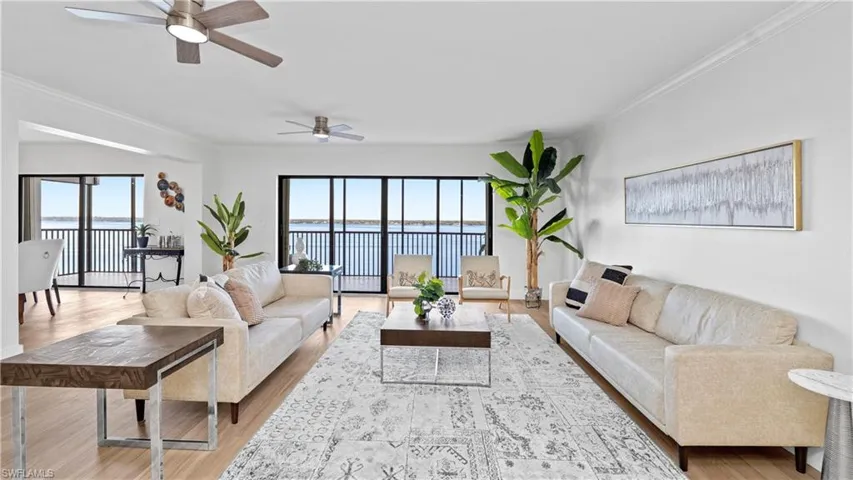 Living room featuring a water view, ornamental molding, a ceiling fan, light wood-type flooring, and plenty of natural light