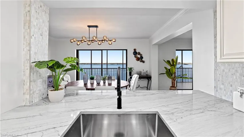 Kitchen featuring tasteful backsplash, light stone countertops, a water view, crown molding, and hanging lights